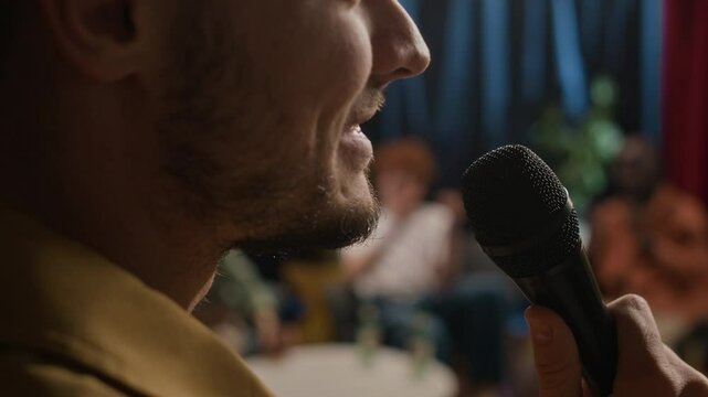 Extreme closeup shot of face of bearded male stand-up comic speaking into microphone and telling jokes, interacting with audience on stage, receiving their applause