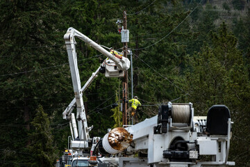 Line crew workman in hydraulic lift bucket, and lineman is climbing gear on wood pole, high up...