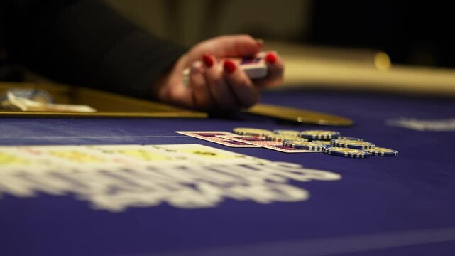 A close up view of a poker game in progress. A player's hand moves across a blue felt table with poker chips stacked and cards spread out.
