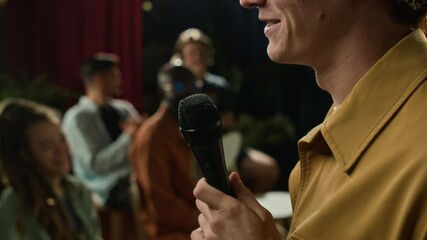 Side cropped shot of face of anonymous male stand-up comedian in yellow shirt and white t-shirt performing on stage, receiving ovation from audience in hall