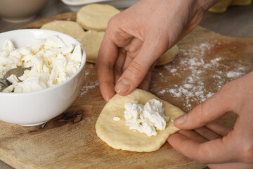 Woman making pirozhki (stuffed pastry pies) with cottage cheese at table, closeup