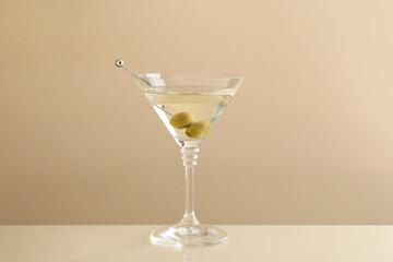 Martini cocktail with olives in glass on beige table