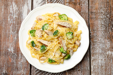 Delicious pasta Alfredo with chicken, cheese and broccoli on wooden table, top view