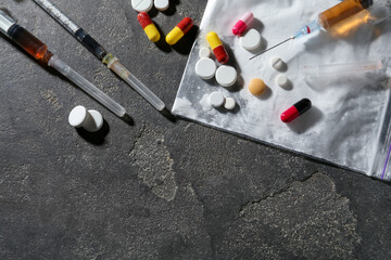 Drug addiction. Plastic bag with powder, syringes and pills on gray textured table, flat lay. Space...
