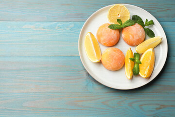 Tasty mochi, cut orange, lemon and mint on light blue wooden table, top view. Space for text