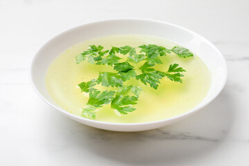 Tasty chicken bouillon in bowl on white marble table, closeup