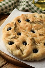 Delicious focaccia bread with olives and rosemary on wooden table, closeup