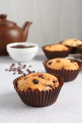 Delicious muffin with chocolate chips on light grey table, closeup