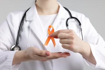 Multiple Sclerosis awareness. Doctor holding orange ribbon on light grey background, closeup