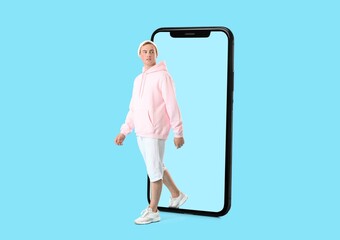 Young man getting out of big mobile phone on blue background. Concept of digital detox