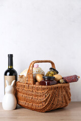 Naklejka premium Basket with Easter eggs, jars, sausage and bottle of wine on wooden table against white background