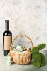 Naklejka premium Basket with Easter eggs, bunnies and bottle of wine on table near grunge wall