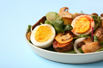Plate of tasty potato salad with eggs and mushrooms on light blue background, closeup