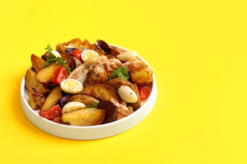 Plate of tasty potato salad with eggs, tomatoes and bacon on yellow background