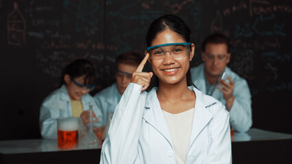 Highschool girl looking at camera while people doing experiment at laboratory. Young cute student...