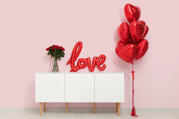 Beautiful roses bouquet with balloon in shape of word LOVE on commode near pink wall. Valentine's...