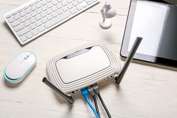 Modern wi-fi router with keyboard and tablet computer on white wooden background