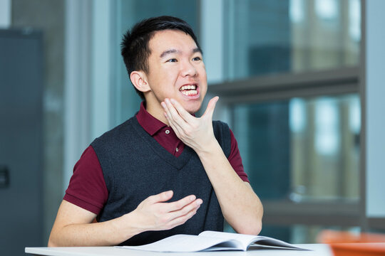 A young teenage boy is doing oral motor exercises in a room. He could be doing singing practice, vocal training, or speech therapy, improving articulation, enunciation and reducing speech impediments