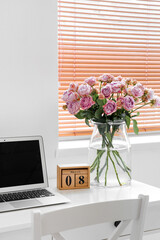 Calendar with date of International Women's Day, roses and laptop on table in office