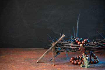 Crown of thorns and nails, beads with cross on rusty table against black grunge background. Good...