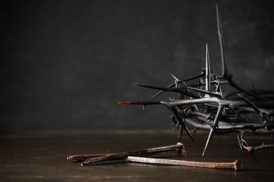Crown of thorns with nails on wooden table against black grunge background, closeup. Good Friday concept