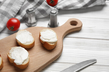 Cutting board of tasty bruschetta with processed cheese and fresh tomatoes on white wooden background, closeup