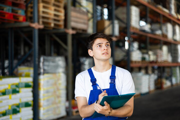In warehouse rack area of store, guy checks availability and quantity of goods and receipt...