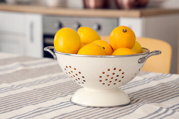 Colander with lemons on dining table in kitchen, closeup
