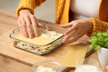 Beautiful mature woman cooking delicious lasagna at table in kitchen, closeup