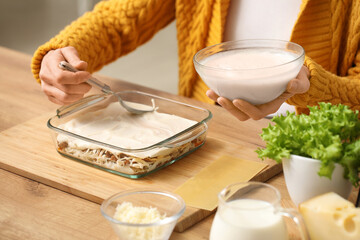 Beautiful mature woman cooking delicious lasagna at table in kitchen, closeup