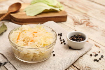 Delicious sauerkraut in bowl with peppercorns on white wooden background. Closeup