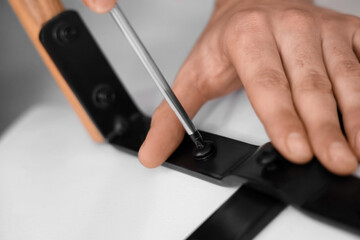 Male carpenter tightening screw in chair with screwdriver, closeup