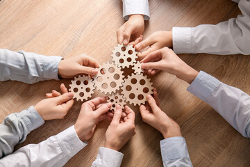 Hands holding wooden gears on wooden background, top view