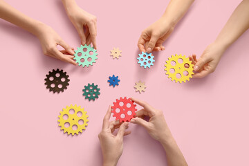 Hands holding wooden gears on pink background, top view