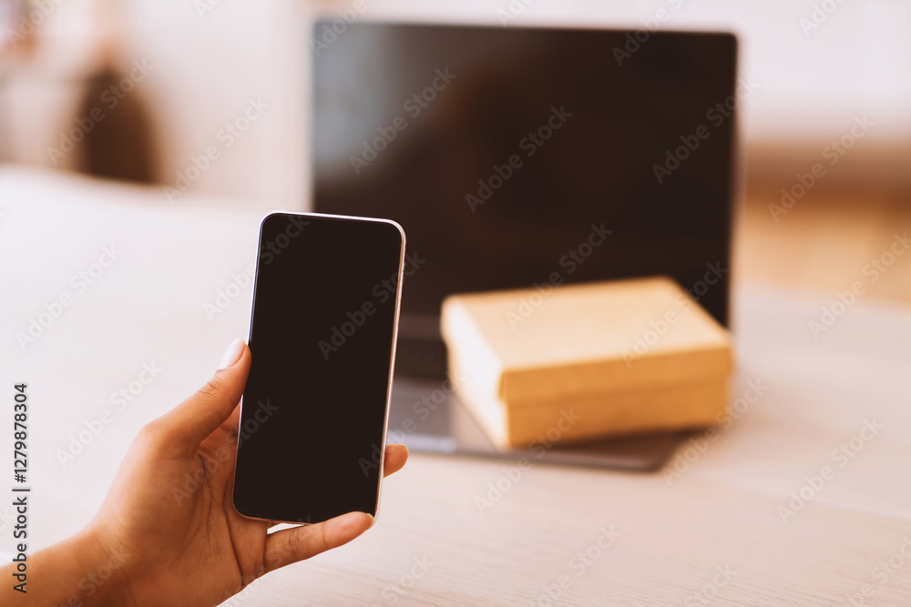 Poster Technology Concept. Unrecognizable black woman holding and showing smartphone with blank empty screen for mock up. Laptop computer with present box or delivery package on keyboard in the background