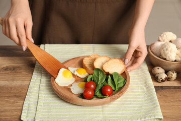 Woman preparing tasty dinner with fried quail eggs, fresh vegetables and toasts in kitchen, closeup