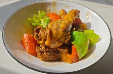 side view of fresh braised chicken with green peppers and orange carrots in the bowl