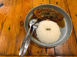 Crispy chicken katsu served with hot rice on a minimalist gray plate and placed on a minimalist wooden table.