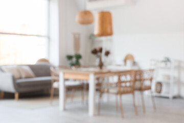 Blurred view of light dining room with table, sofa and shelf units