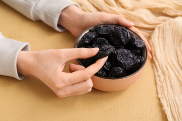 Female hands with bowl of dried prunes on beige background