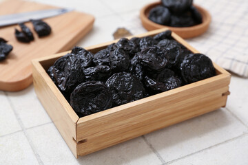 Wooden box with dried prunes on white tile background