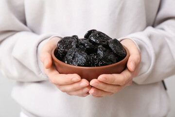 Woman holding bowl with dried prunes on grey background, closeup