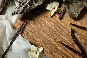 Frame made of vanilla sticks, flowers, tree bark and fabric on wooden background, closeup