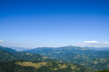 Mountainous landscape featuring rolling green hills, dense forestry, and clear, expansive blue sky. Carpathian Mountains, Ukraine