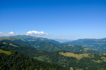 Mountainous landscape featuring rolling green hills, dense forestry, and clear, expansive blue sky....