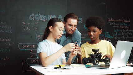 Caucasian teacher looking at laptop screen while explain car model system at blackboard with coding...