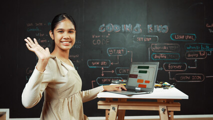 Smart highschool girl waving to camera while programing code at blackboard with engineering code or...