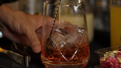 Cropped closeup hand bartender stirring mixed ingredients alcohol liquor syrup into mixing glass with cube ice prepared Old fashioned cocktail tasting showcasing nightlife mixology at bar. Vinosity.