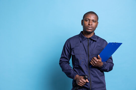 Serious security guard holding his baton weapon and papers in studio against blue background, using files to keep track of all responsibilities on the job. Trained agent protecting the area.