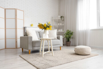 Interior of living room with sofa, shelf unit and mimosa flowers in vase
